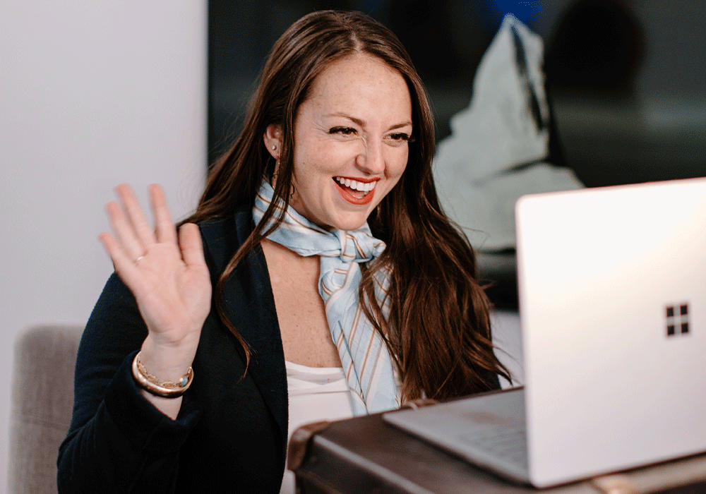 Woman smiling and waiving at her laptop while on a video call.