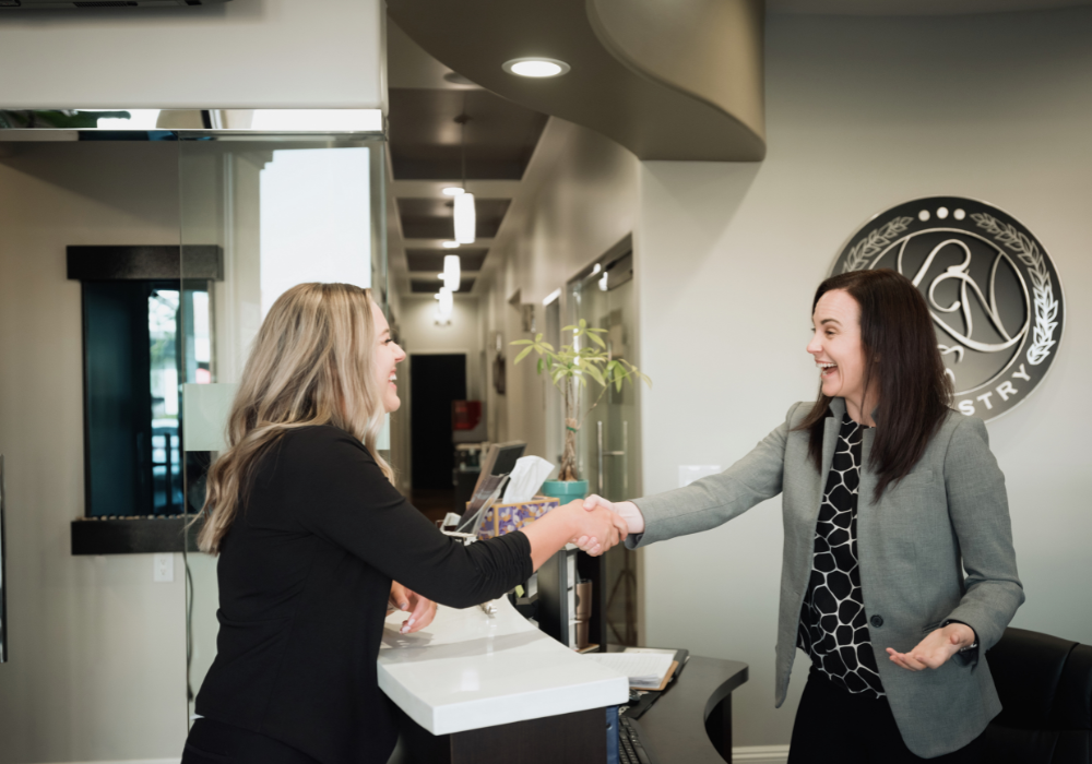 Interviewer and an applicant shaking hands over the counter at the dental office